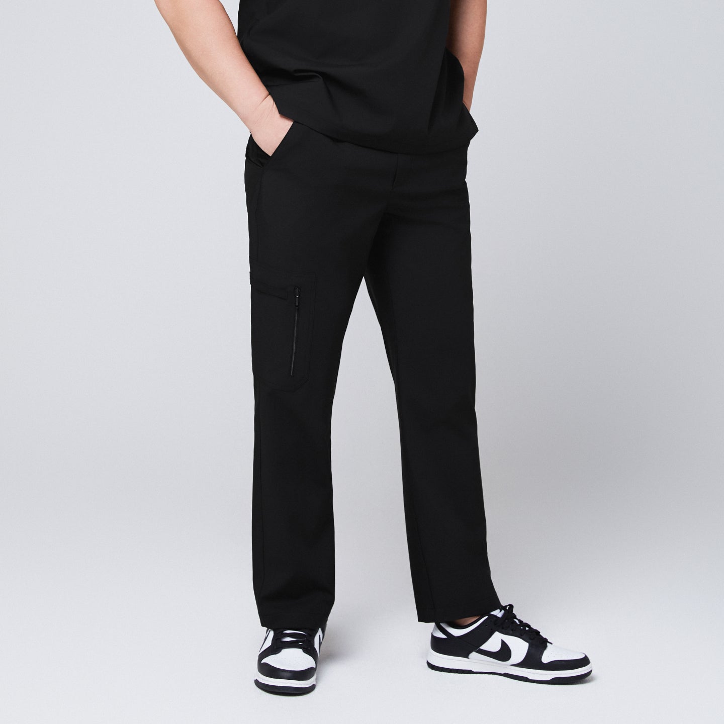 Image of A male model wearing black straight scrub pants with a zipper pocket, paired with a matching scrub top and sneakers,Eco Black